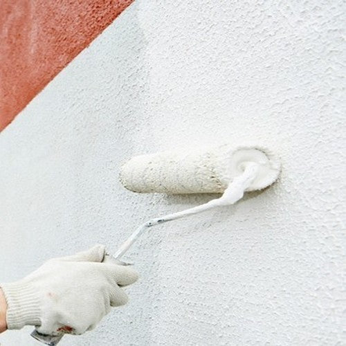 Application de peinture blanche au rouleau sur un mur texturé, à côté d'une bande rouge