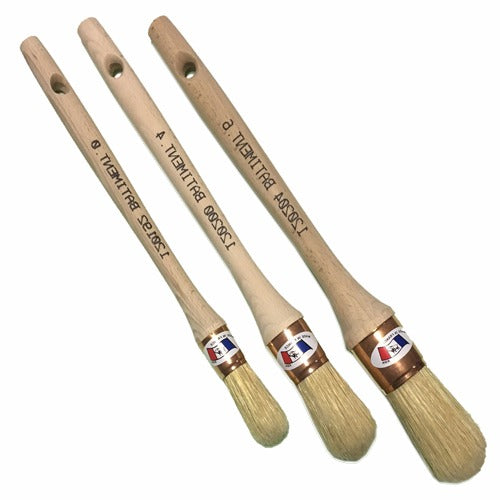 Trois pinceaux à manche en bois et poils naturels clairs, de tailles différentes, sur fond blanc