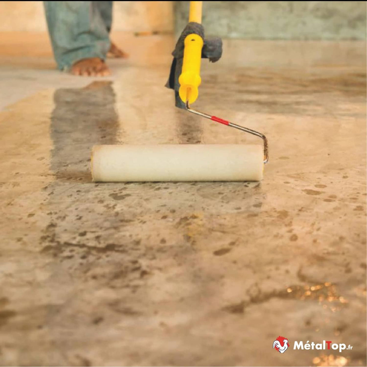 Application d'un produit au rouleau à peindre sur un sol en béton, par un ouvrier pieds nus