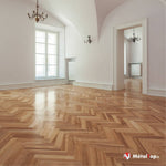 Parquet en chevrons en bois clair dans une pièce vide aux murs blancs, avec lustre et fenêtre