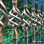 Grille en fer forgé à volutes torsadées dorées sur fond de feuillage vert