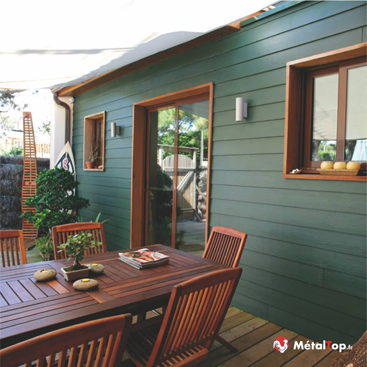 Façade de maison en bardage vert foncé, terrasse en bois avec mobilier de jardin en teck