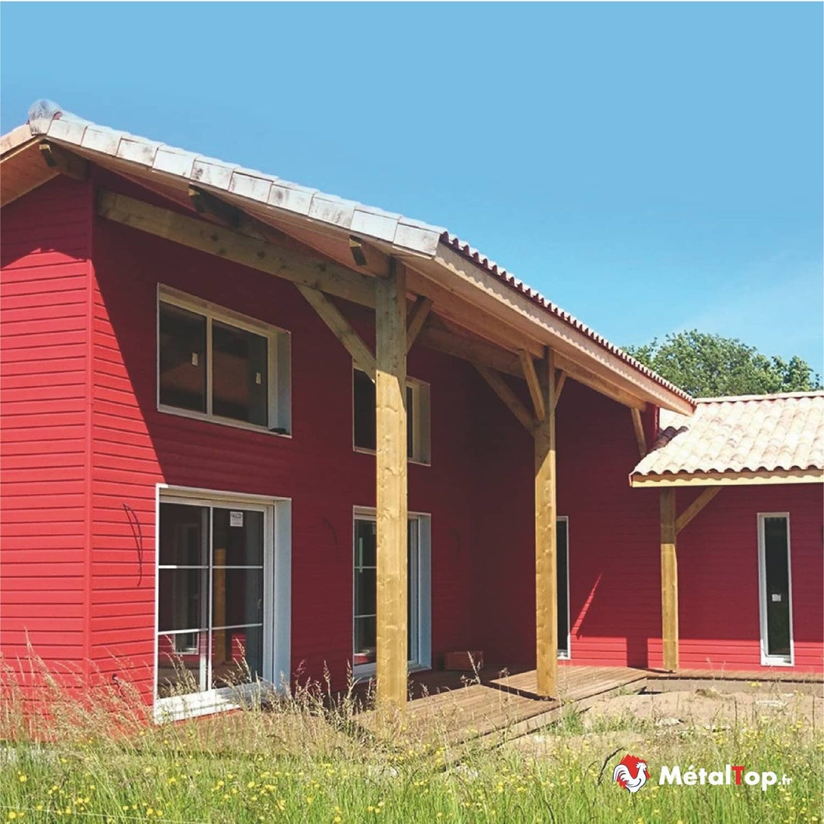 Maison à façade rouge avec poteaux et charpente en bois, toiture en tuiles et terrasse en bois