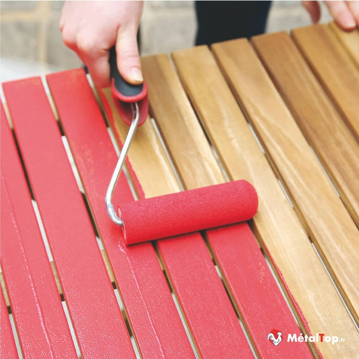 Application d'une peinture rouge au rouleau sur des lames de bois naturel