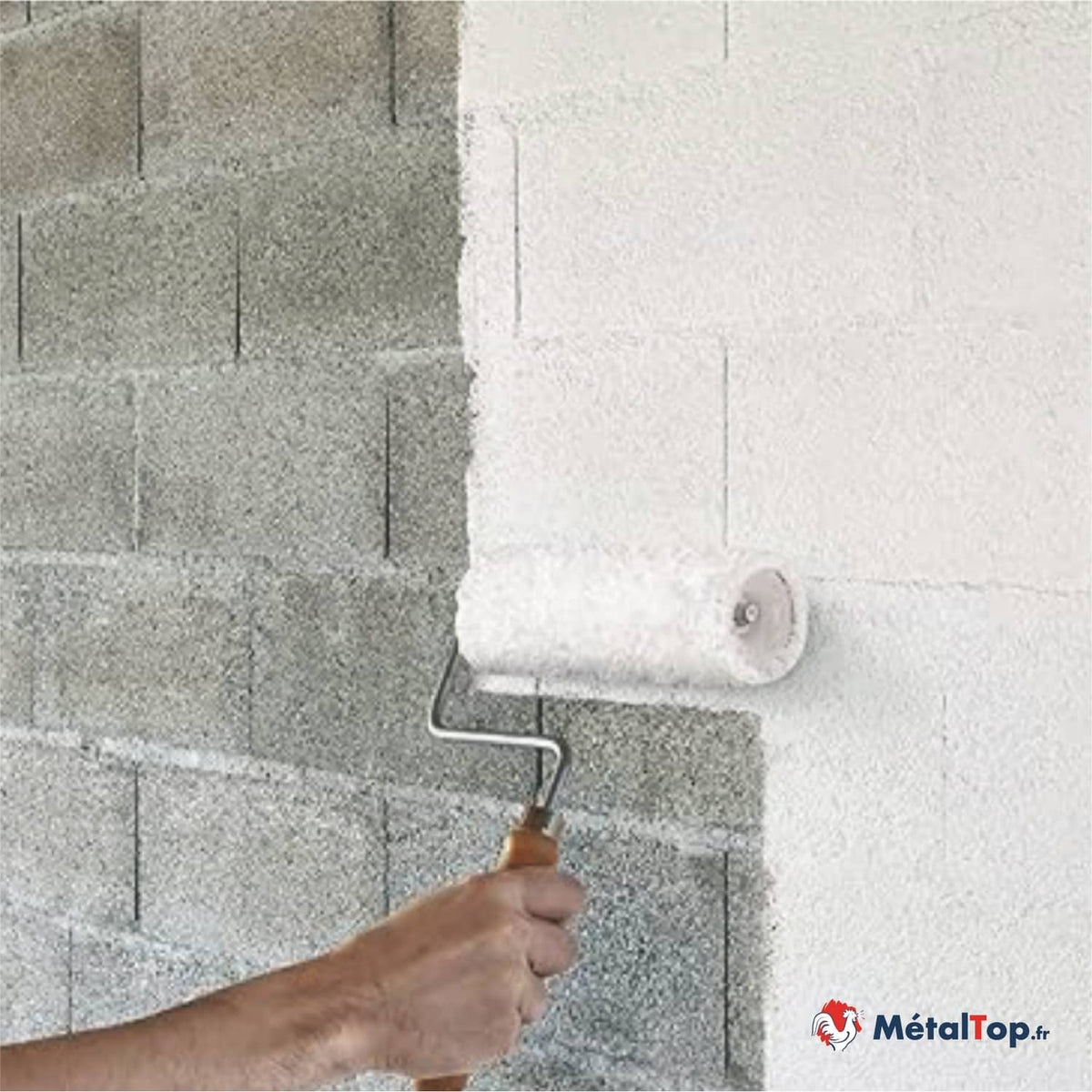Application de peinture blanche au rouleau sur un mur en parpaings gris