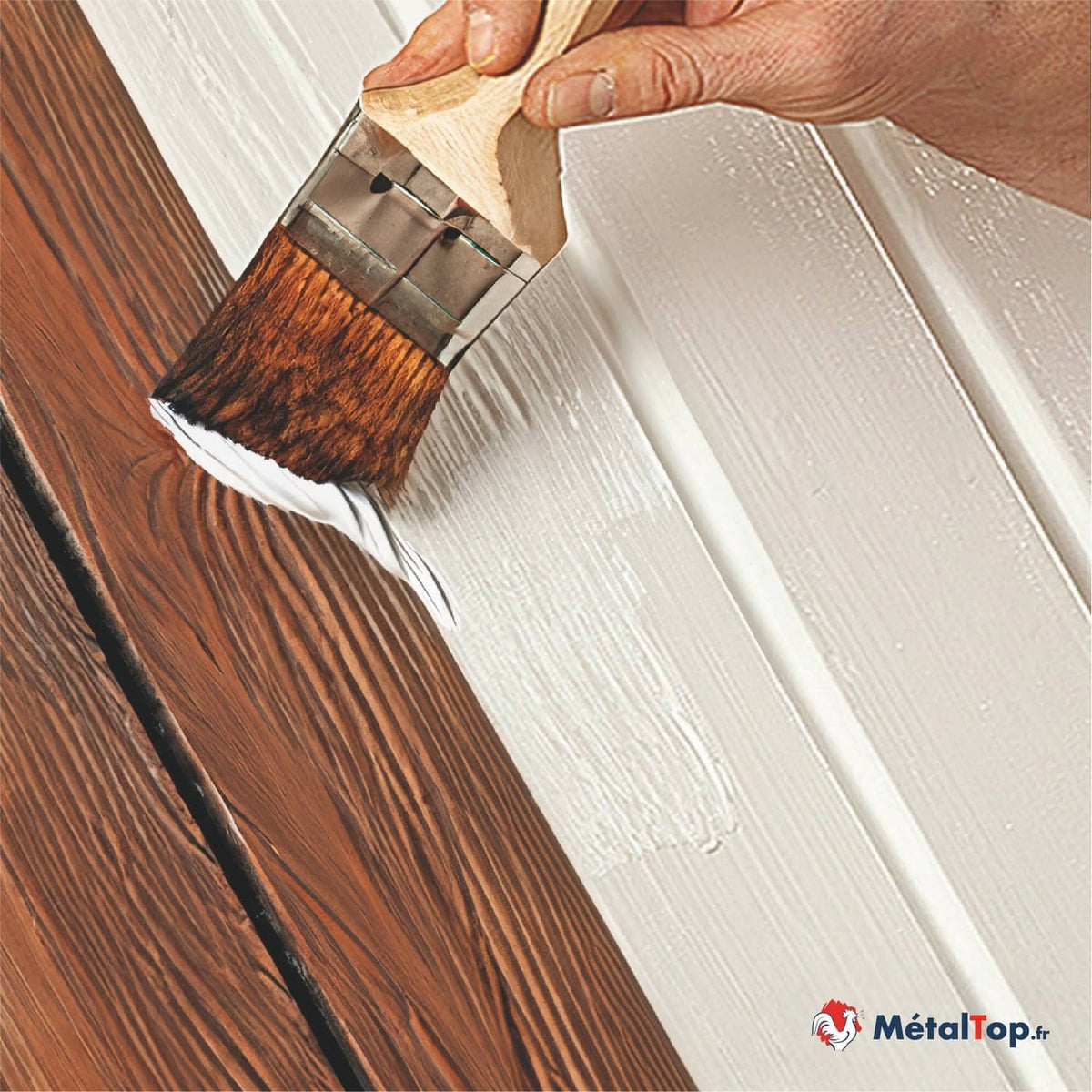 Pinceau appliquant de la peinture blanche sur une planche de bois brun aux veines apparentes