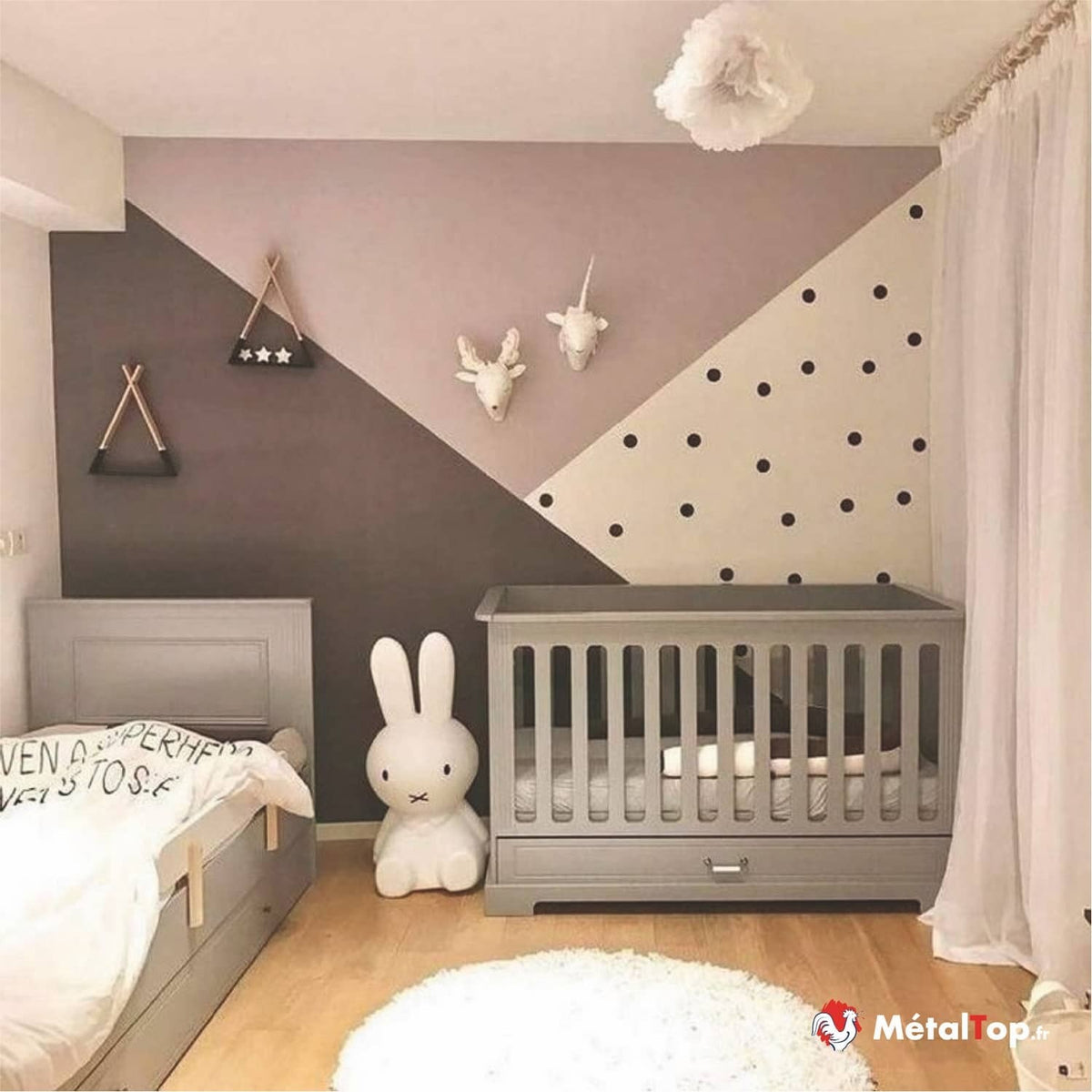 Chambre d'enfant avec lits gris, mur à motifs géométriques rose, taupe et pois noirs, lapin blanc