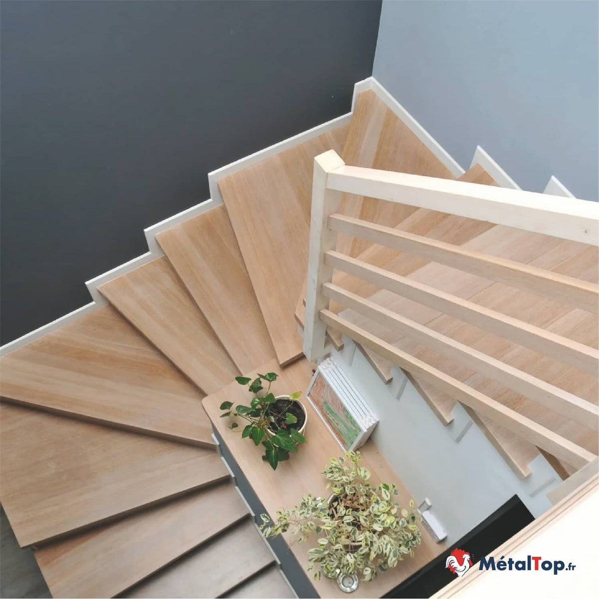 Escalier tournant en bois clair avec garde-corps en bois et plantes vertes sur le palier