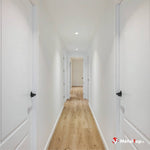 Couloir lumineux avec portes blanches, murs blancs et sol en parquet clair