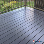 Terrasse en bois peinte en gris anthracite avec balustrade métallique marron et jardin verdoyant