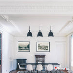 Salle à manger au plafond mouluré avec table noire, chaises blanches et trois suspensions noires