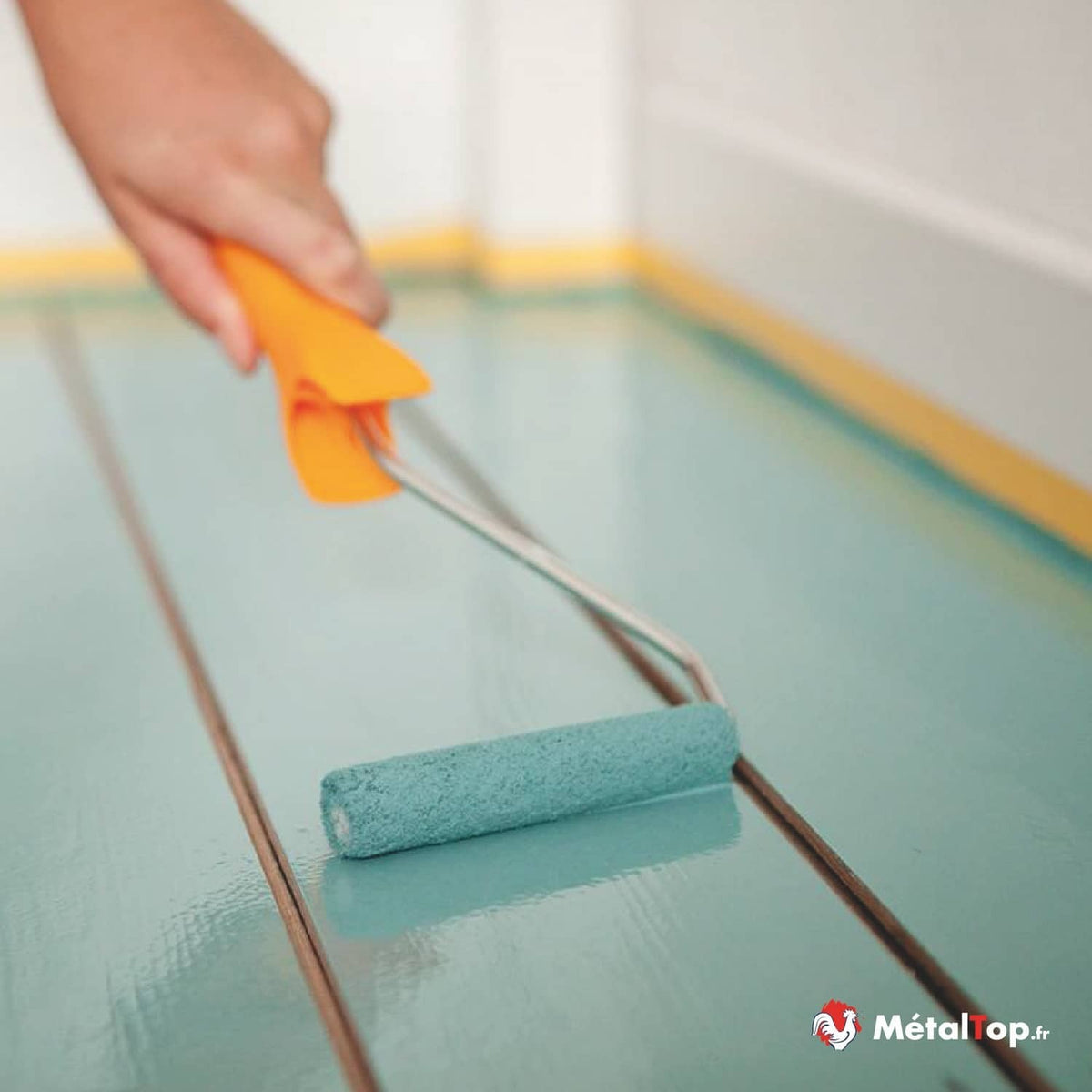 Peinture turquoise appliquée au rouleau sur un plancher en bois, près de plinthes jaunes