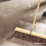 Balai-brosse à manche en bois balayant un sol gris humide couvert de mousse blanche