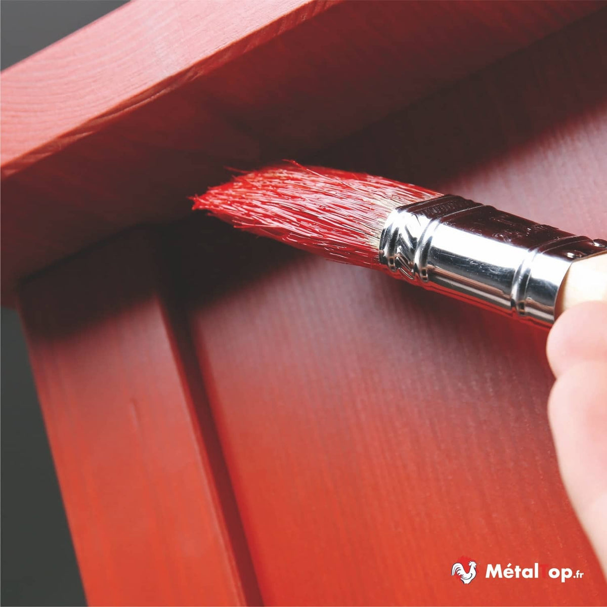 Pinceau plat chargé de peinture rouge appliquée sur un panneau de bois rouge