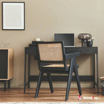 Bureau noir avec chaise en cannage, lampe en verre fumé et cadre mural sur mur beige