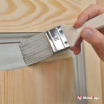 Pinceau plat de 2 pouces appliquant une peinture grise sur un cadre en bois de pin