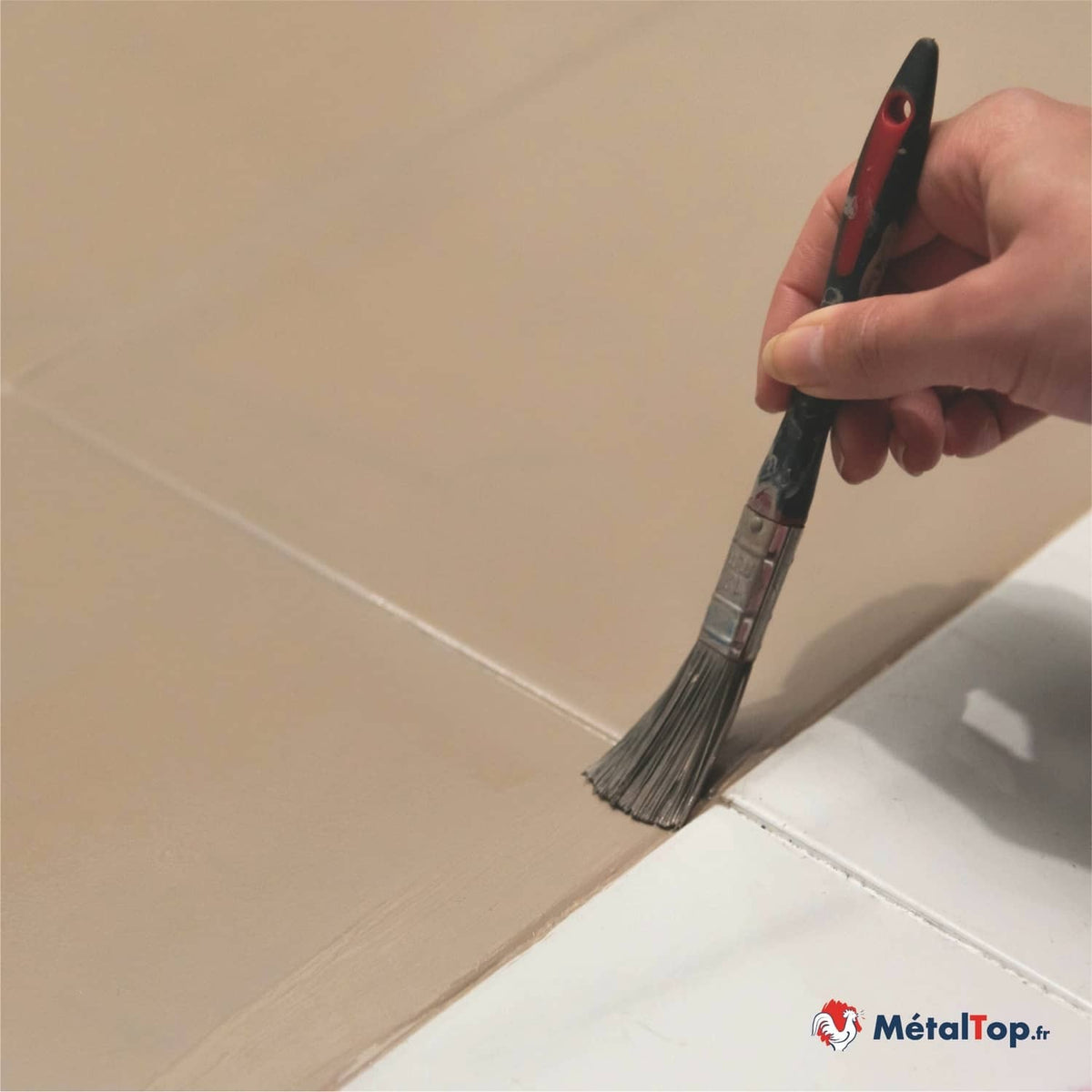 Pinceau appliquant de la peinture beige sur un carrelage, à côté de carreaux blancs