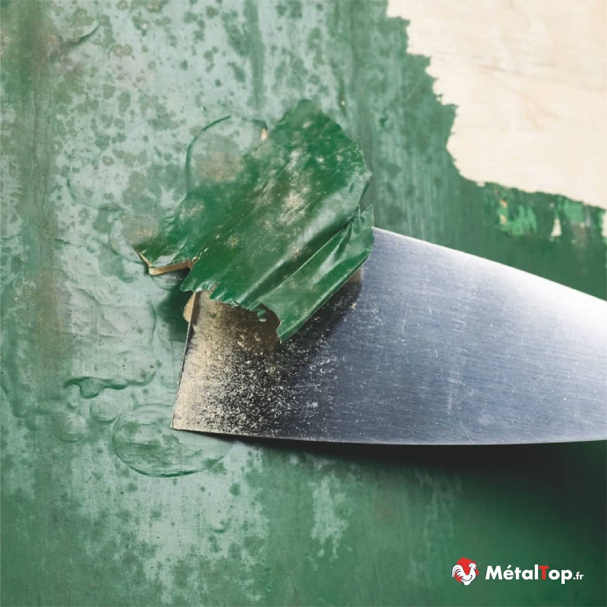 Spatule en acier décapant une peinture verte écaillée sur une surface métallique