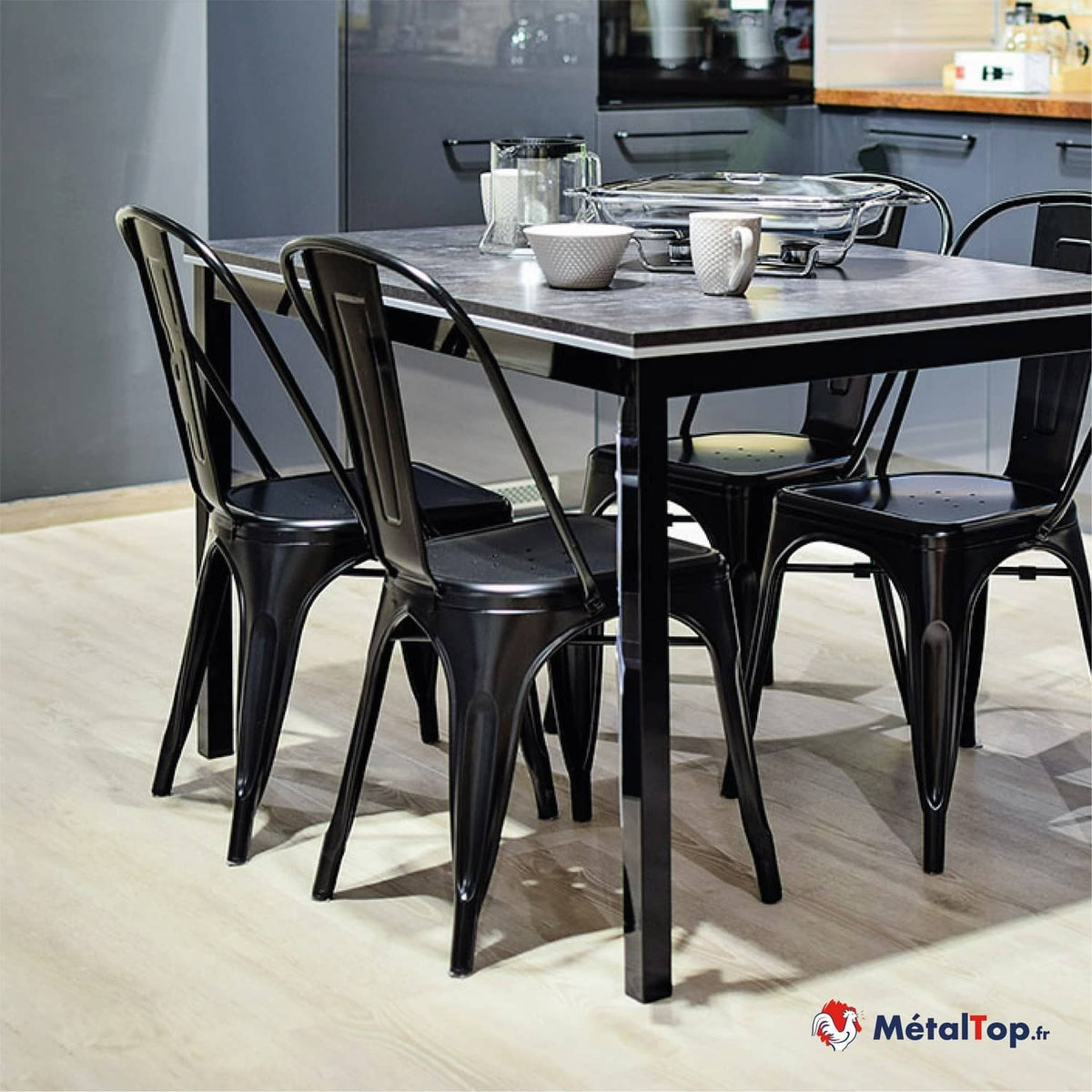 Chaises en métal noir autour d'une table de cuisine au plateau gris, avec vaisselle en verre et céramique