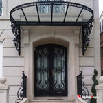 Porte cintrée en fer forgé noir sous auvent en verre à ferronnerie, façade en pierre claire