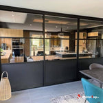 Verrière à structure noire séparant une salle à manger d'une cuisine moderne en bois clair