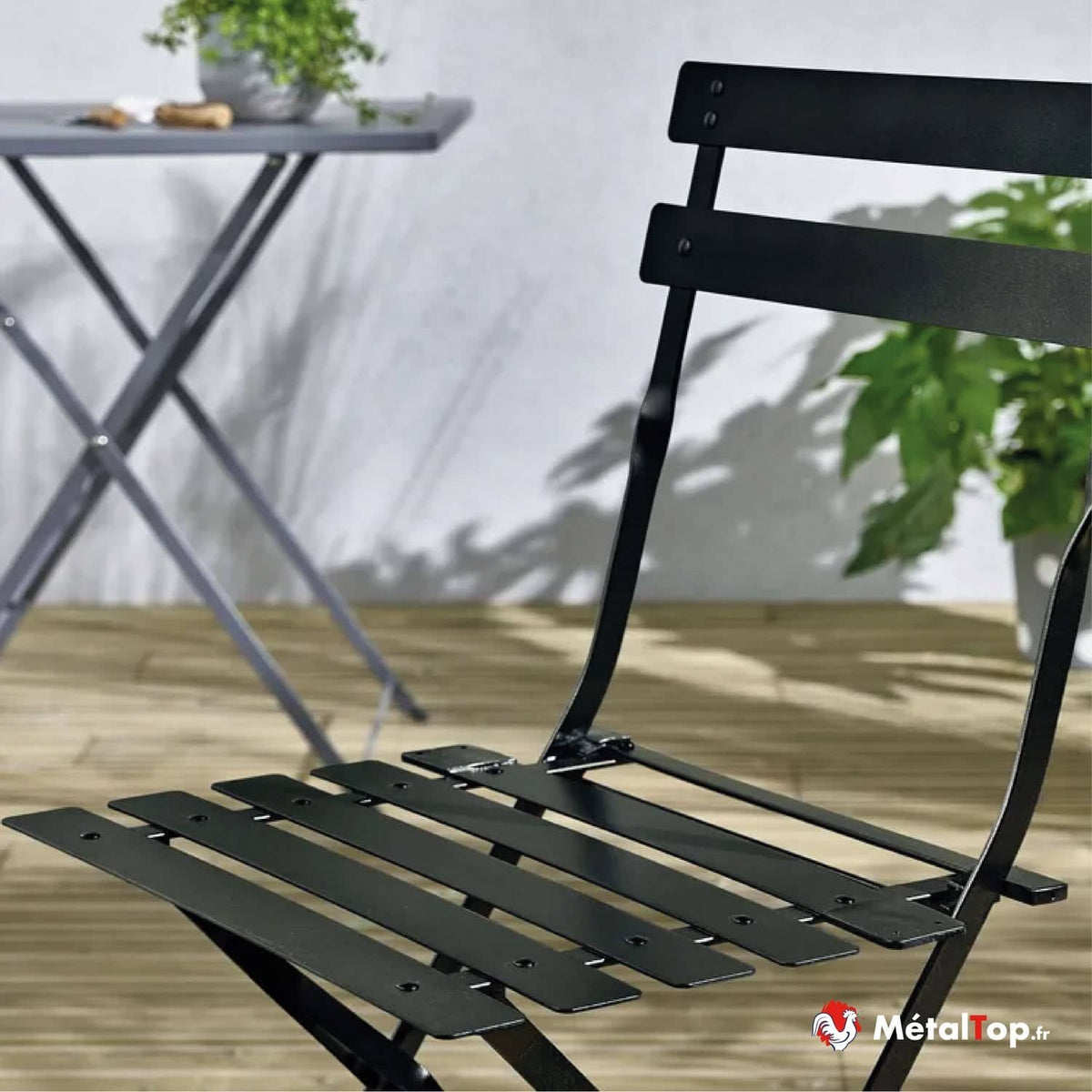Chaise de jardin pliante en métal noir sur terrasse en bois, avec table grise en arrière-plan