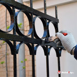 Application de peinture noire au pinceau sur une grille en fer forgé à motifs circulaires