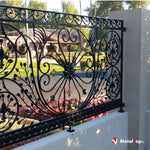 Grille en fer forgé noir avec volutes, fleurs de lys et motifs floraux sur muret blanc