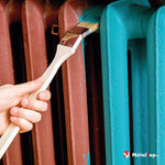 Radiateur en fonte en cours de peinture au pinceau, passant du rouge au turquoise