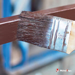 Pinceau plat appliquant une peinture marron sur une barre métallique