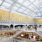 Verrière et ferronnerie blanches, fresques jaunes aux paons et visiteurs dans un grand magasin