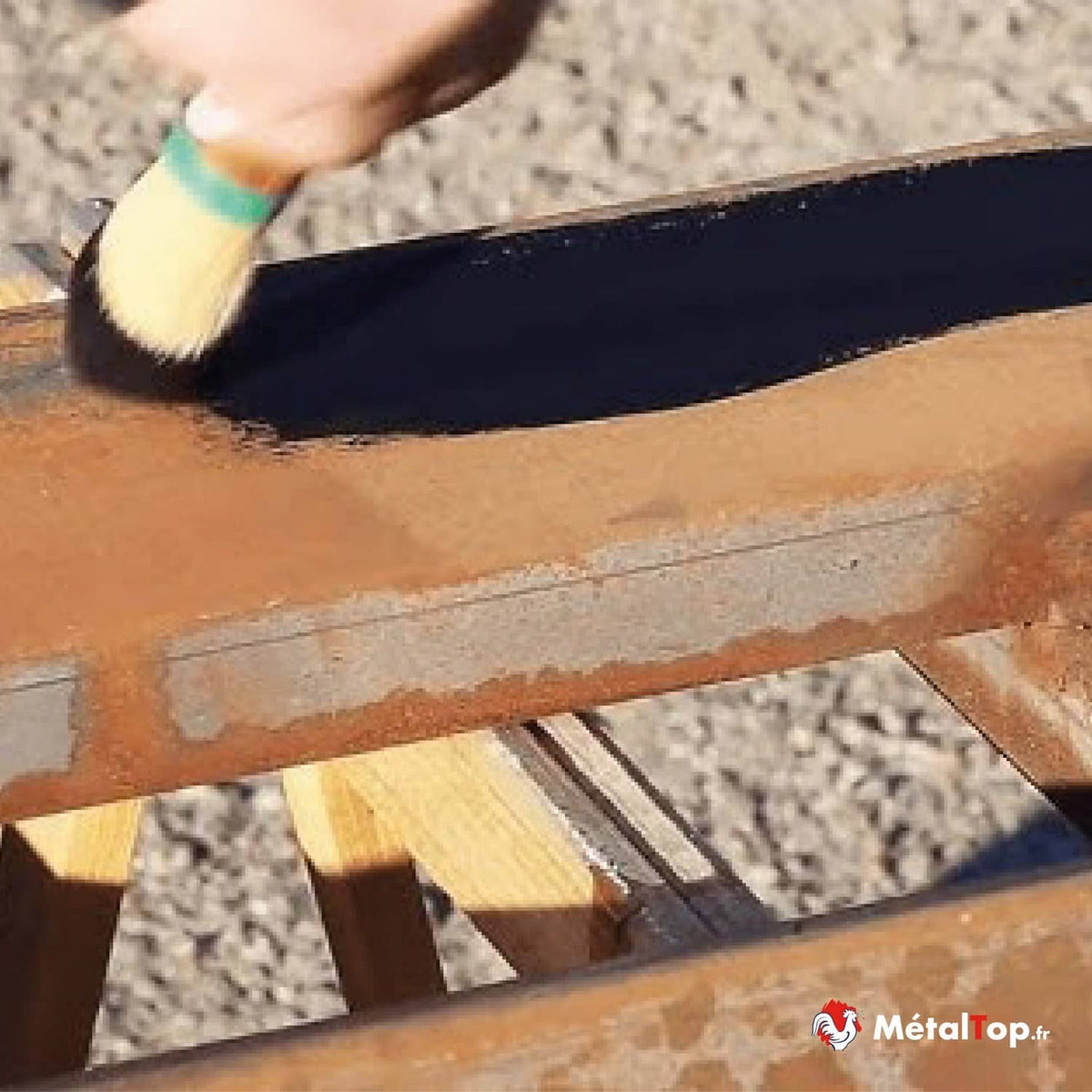 Application de peinture noire au pinceau sur une poutre métallique rouillée au-dessus de lames en bois