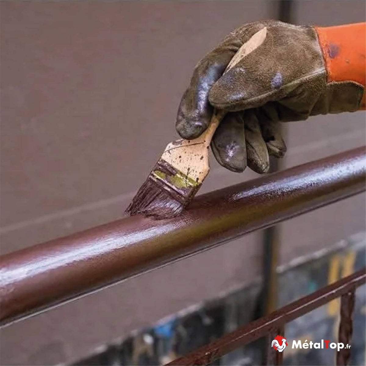 Application de peinture marron au pinceau sur une rampe métallique, avec gants de travail