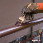 Application de peinture marron au pinceau sur une rampe métallique, avec gants de travail