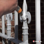 Peinture blanche appliquée sur une grille en fer forgé ornée de fleurons décoratifs