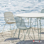 Chaises en métal ajourées et table ronde blanche sur une terrasse en bois au bord de l'eau