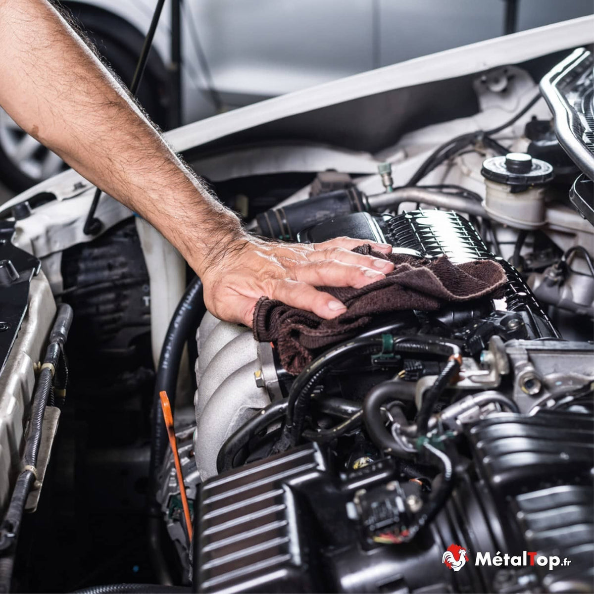 Nettoyage d'un moteur de voiture avec un chiffon, capot ouvert