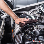 Nettoyage d'un moteur de voiture avec un chiffon, capot ouvert