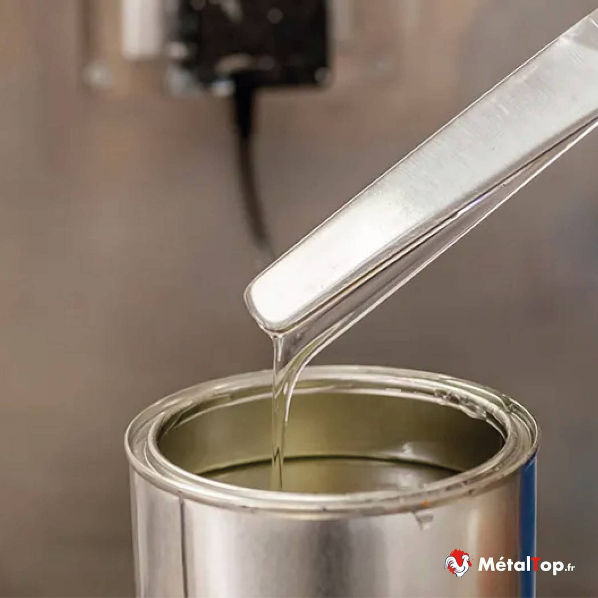Peinture liquide coulant d'une spatule métallique dans un pot de peinture ouvert