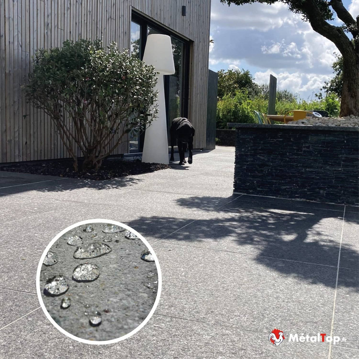 Terrasse en dalles grises avec gouttes d'eau déperlantes, muret en ardoise et maison en bois