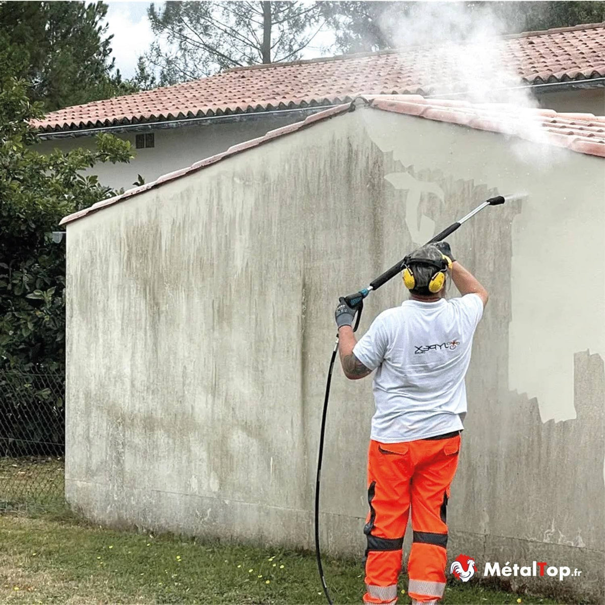 Ouvrier en tenue haute visibilité nettoyant une façade au nettoyeur haute pression