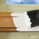 Application de peinture blanche au pinceau sur une moulure en bois brun, protégée par du ruban de masquage
