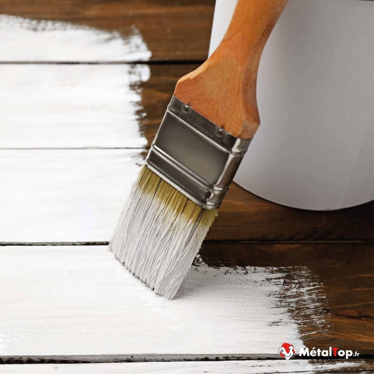 Pinceau plat appliquant de la peinture blanche sur un plancher en bois foncé