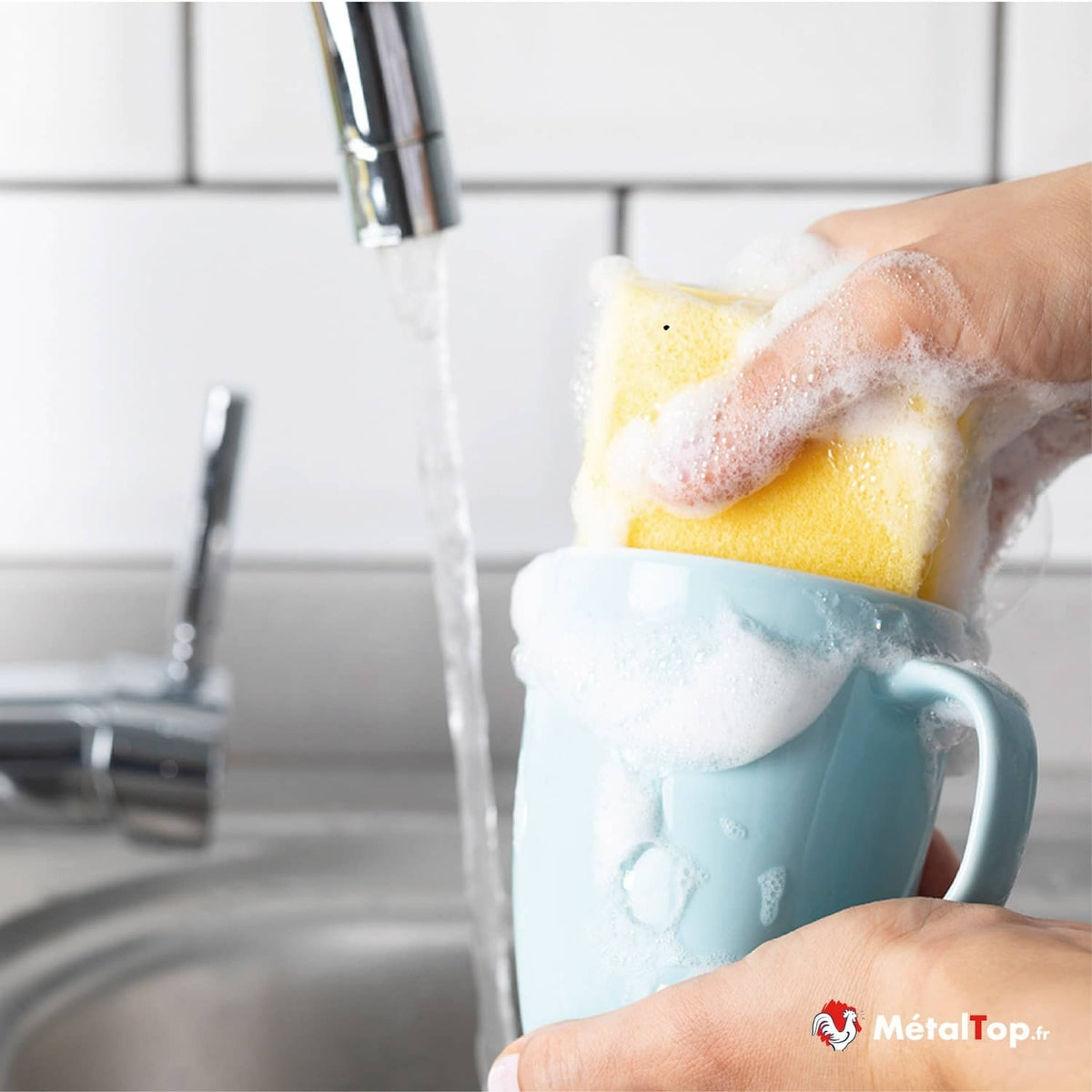 Tasse bleue couverte de mousse, lavée avec une éponge jaune sous un robinet d'eau courante