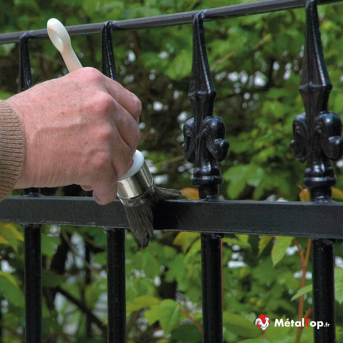 Peinture noire appliquée au pinceau sur une grille en fer forgé à pointes décoratives