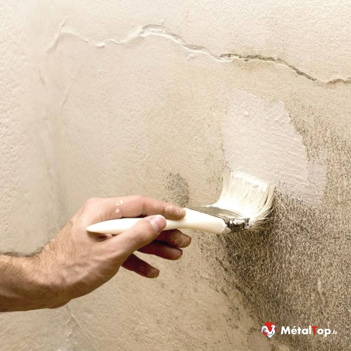 Application d'une peinture blanche au pinceau sur un mur beige fissuré et taché