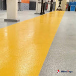 Sol industriel gris avec bande de circulation jaune brillante entre piliers blancs