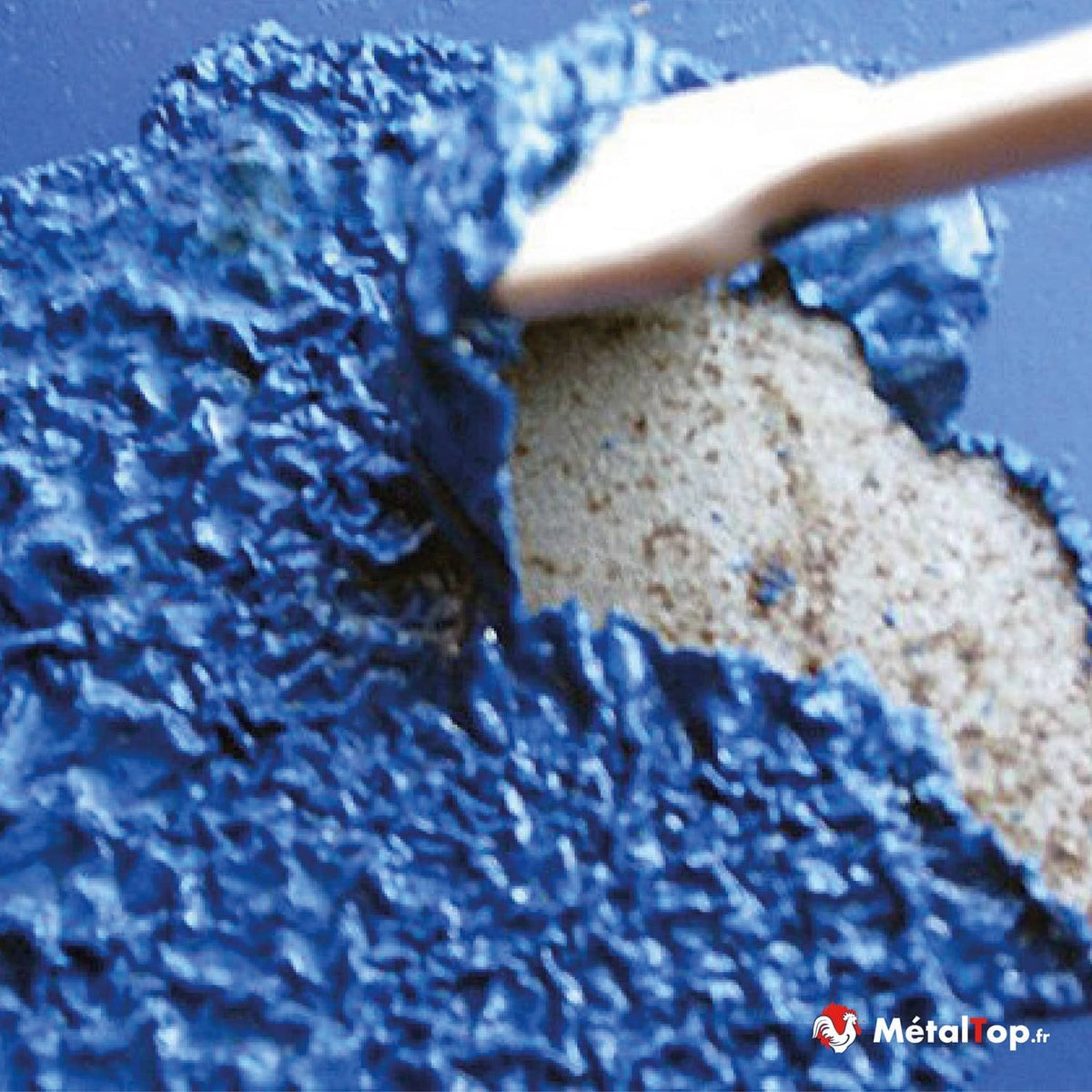 Poudre granulée bleue écartée par une spatule, révélant une poudre beige en dessous