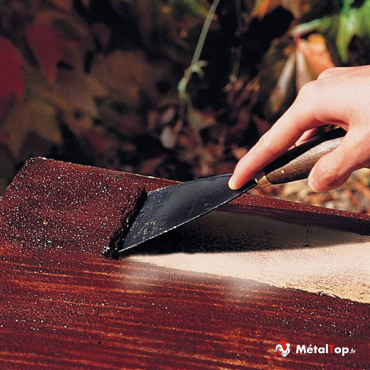 Application d'enduit de rebouchage au couteau sur une surface en bois brun-rouge