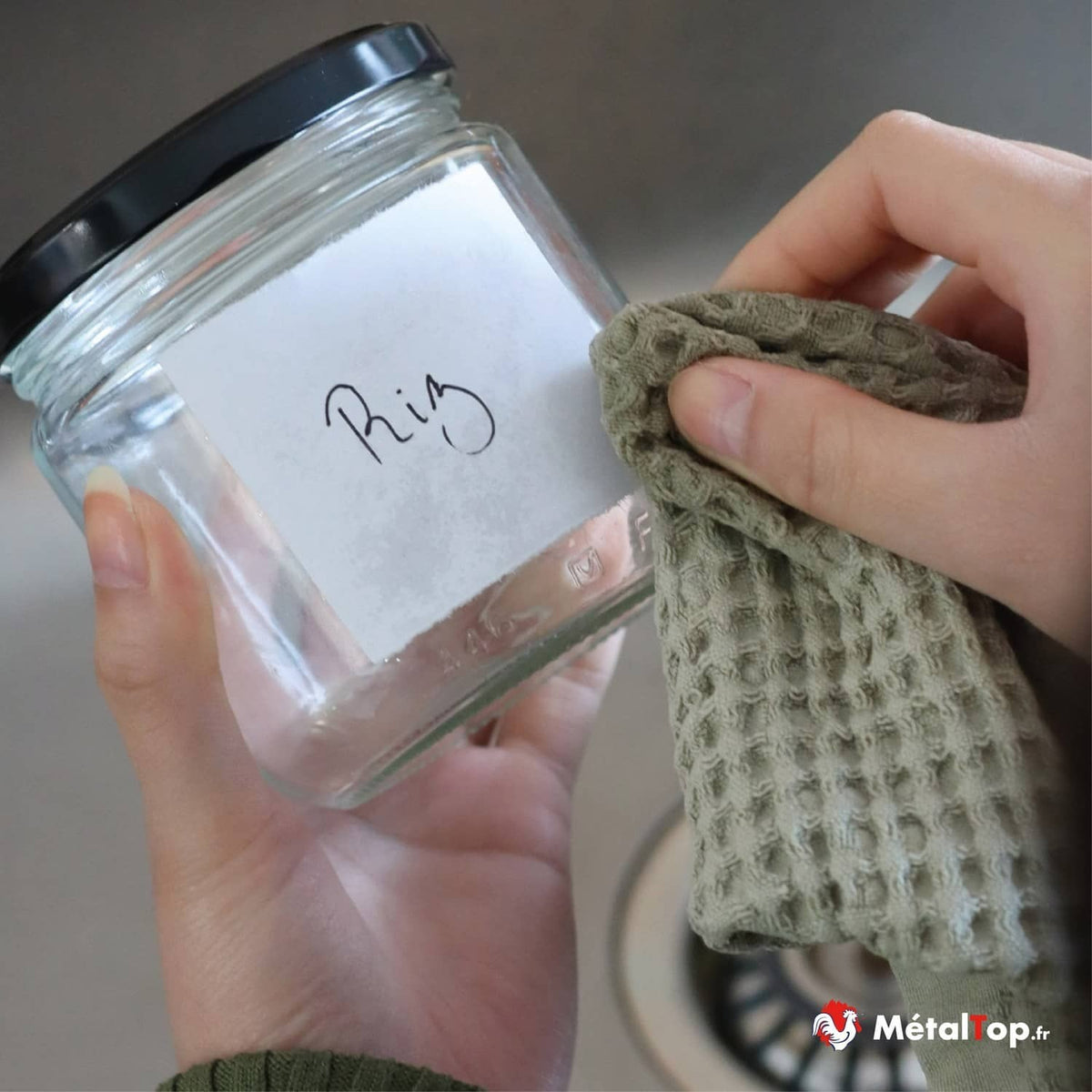 Pot en verre à couvercle noir étiqueté « Riz », essuyé avec un torchon vert kaki